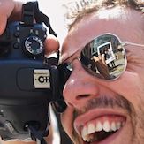 Photographer wearing sunglasses - smiling and holding a camera to his eye.