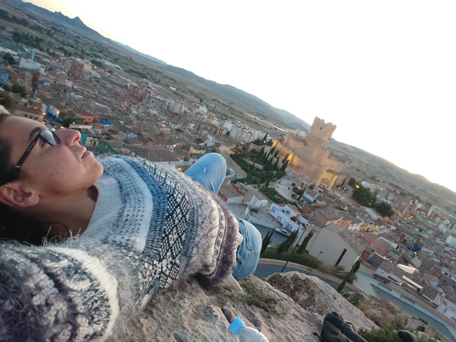 Student lying down on top of a hill with a view of a Spanish city in the background