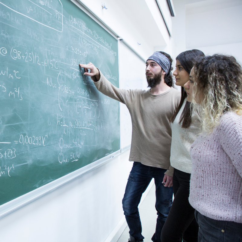 3 students looking at maths problem on chalkboard - mathematics student blog