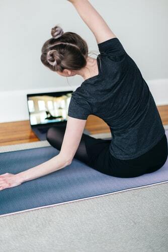A woman stretching on a yoga mat, watching an online class. 