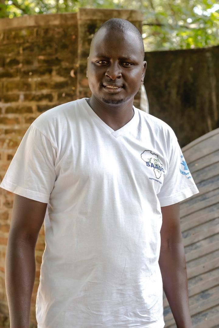A photograph of Elijah Manyok infront of a brick wall