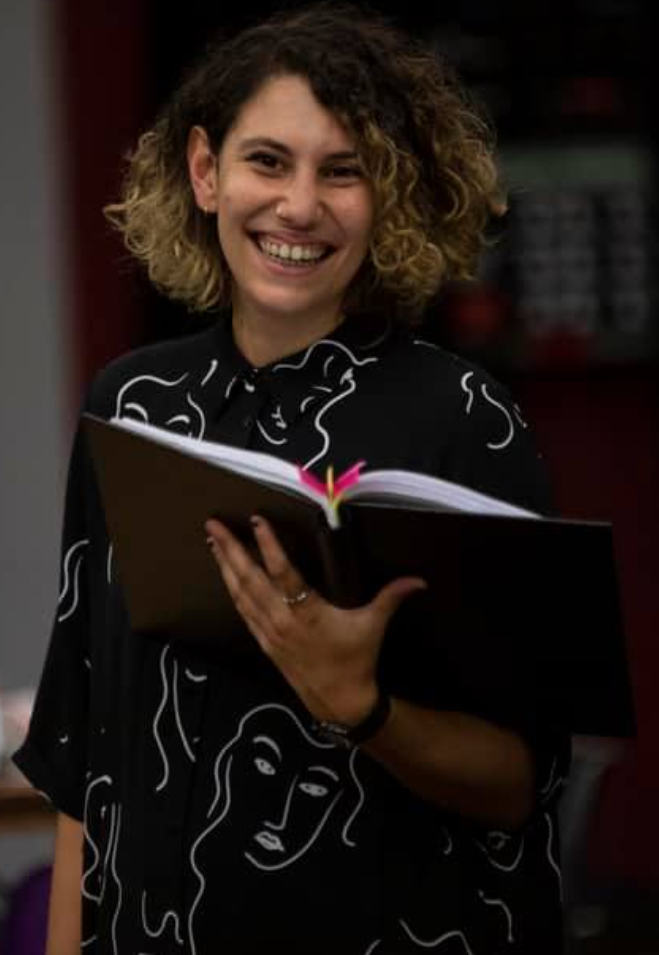 a Photograph of Emilie holding a book open in one hand, smiling