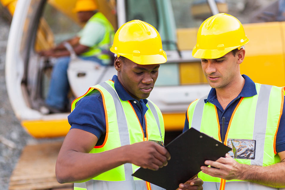 Two males working on construction site looking at clipboard