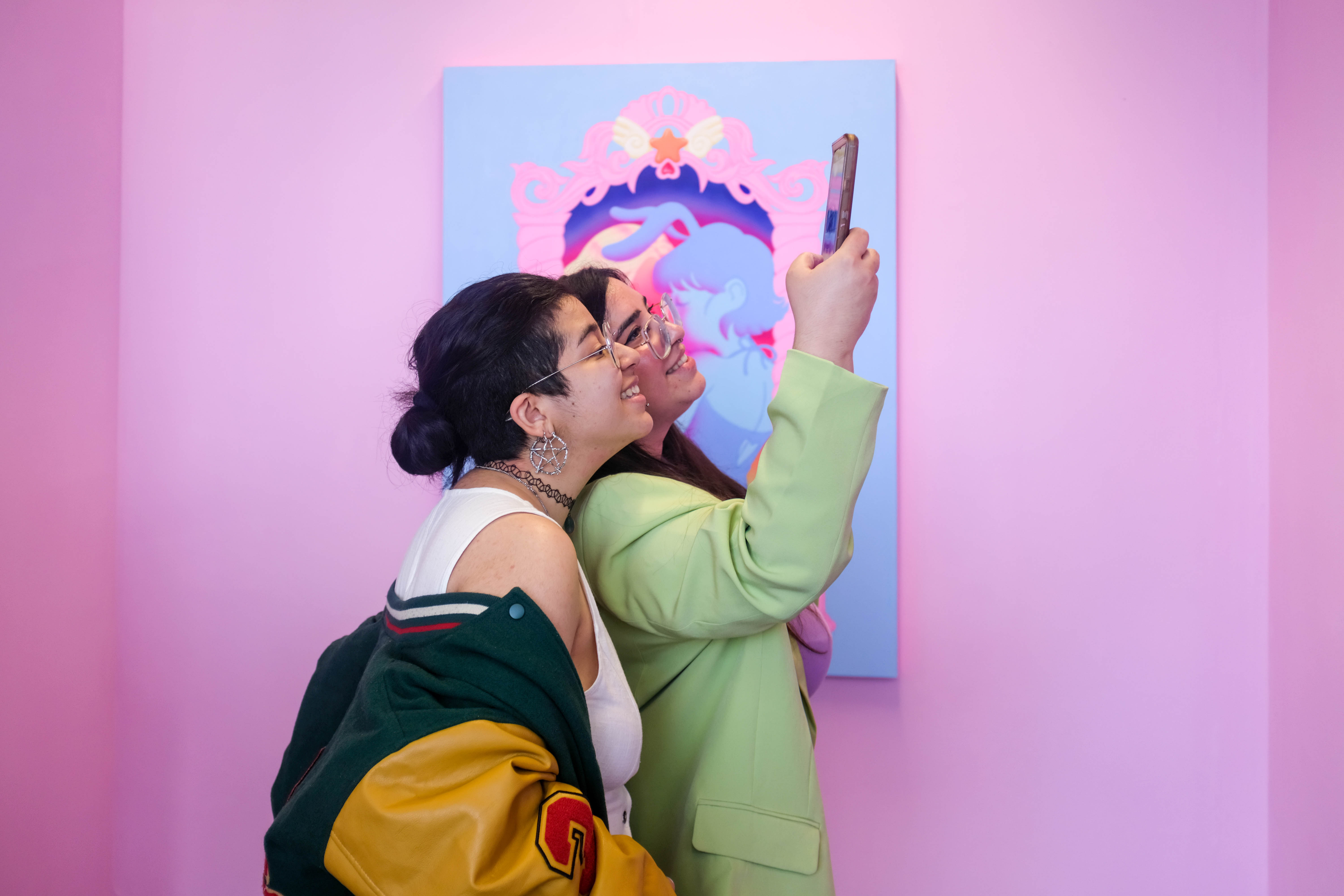 Image of two girls stood in a gallery space at the University of Salford degree show taking a photo of artwork