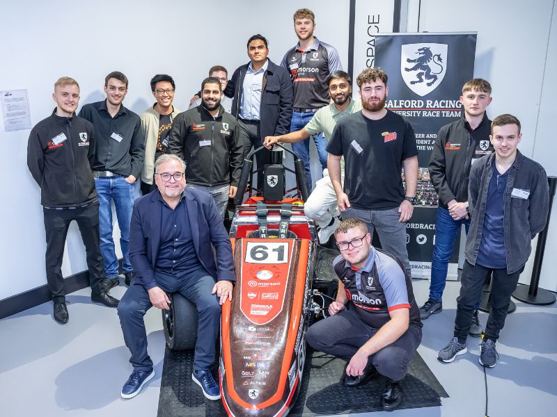 a large group of students and an industry partner stand around a racing car