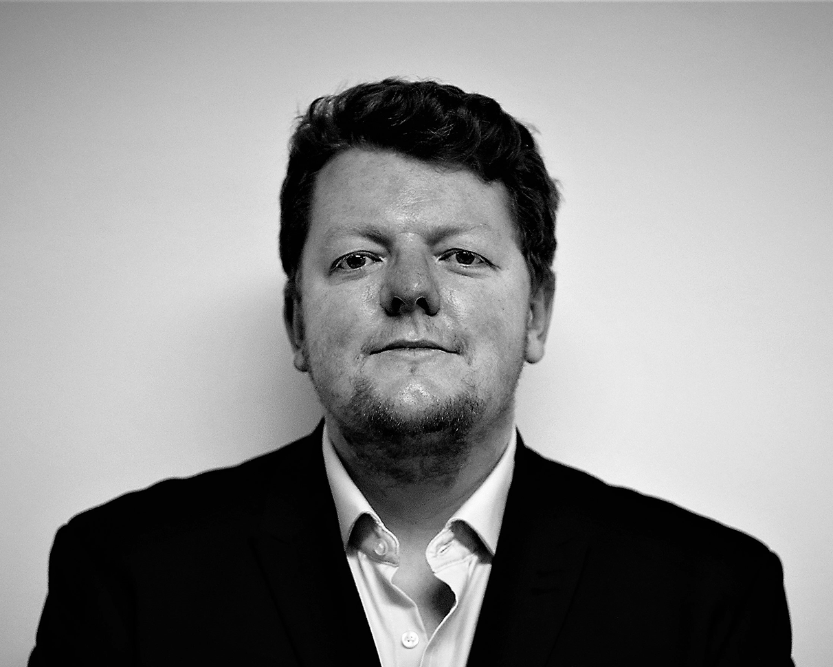 Black and white headshot of a man in a white shirt and black jacket. 