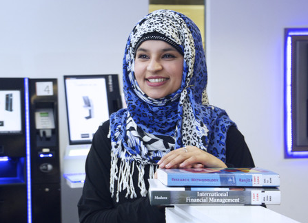 Student standing and smiling, leaning on a pile of business books