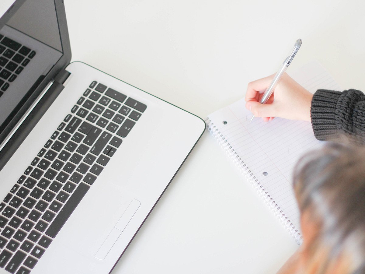 Person working at a laptop writing notes on paper