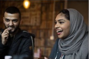 man with hand to mouth and woman in head scarf laughs