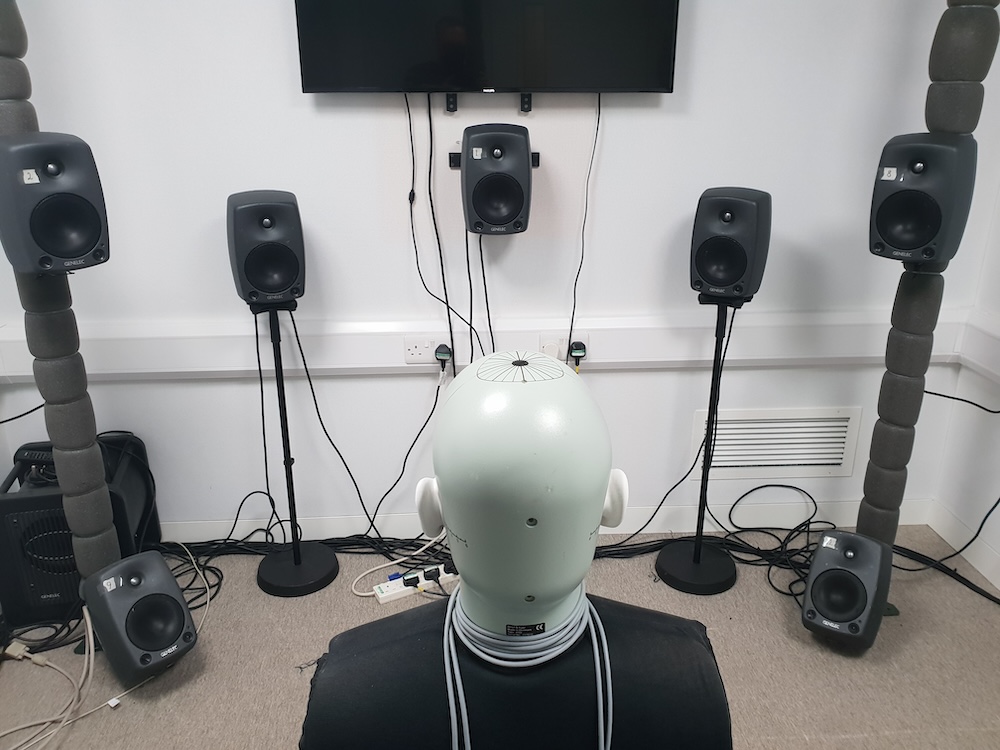 Head and torso simulator dummy in a room surrounded by audio monitors
