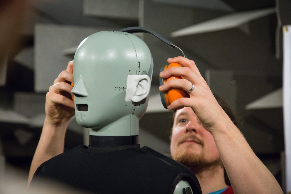a person placing ear defenders on head and torso simulator dummy