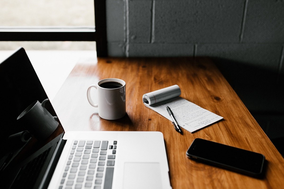 Workspace with laptop, desk, notepad, phone and coffee