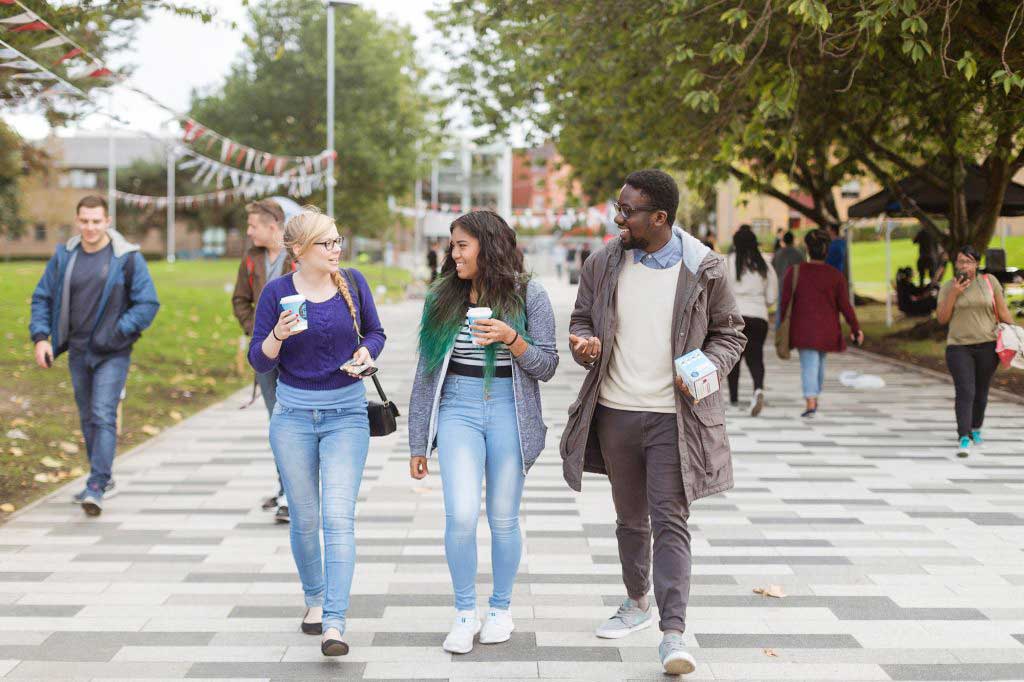 Three students walking along the broadwalk path on University of Salford Peel Park campus