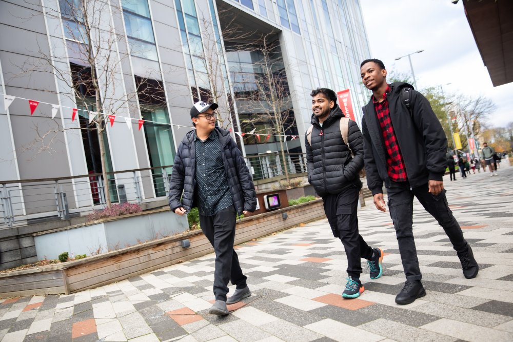 Three students walking through campus in front of New Adelphi