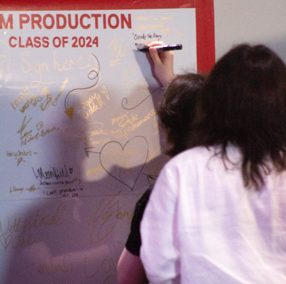 Two students write messages on a white board for Film Production Class of 2024