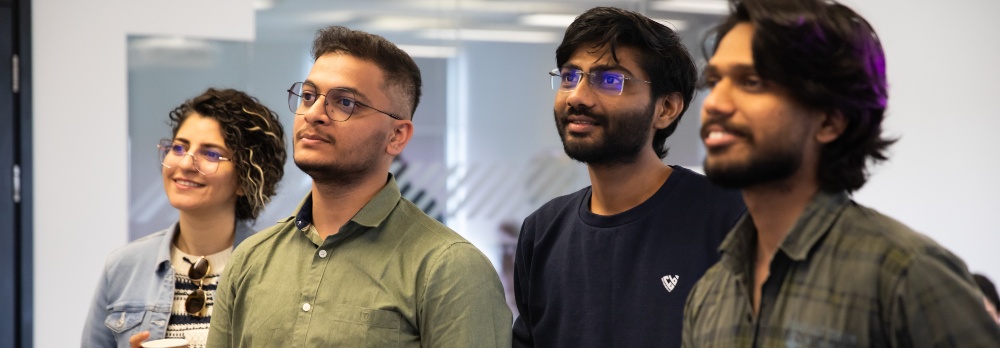 Four students stood in a row looking at something off camera