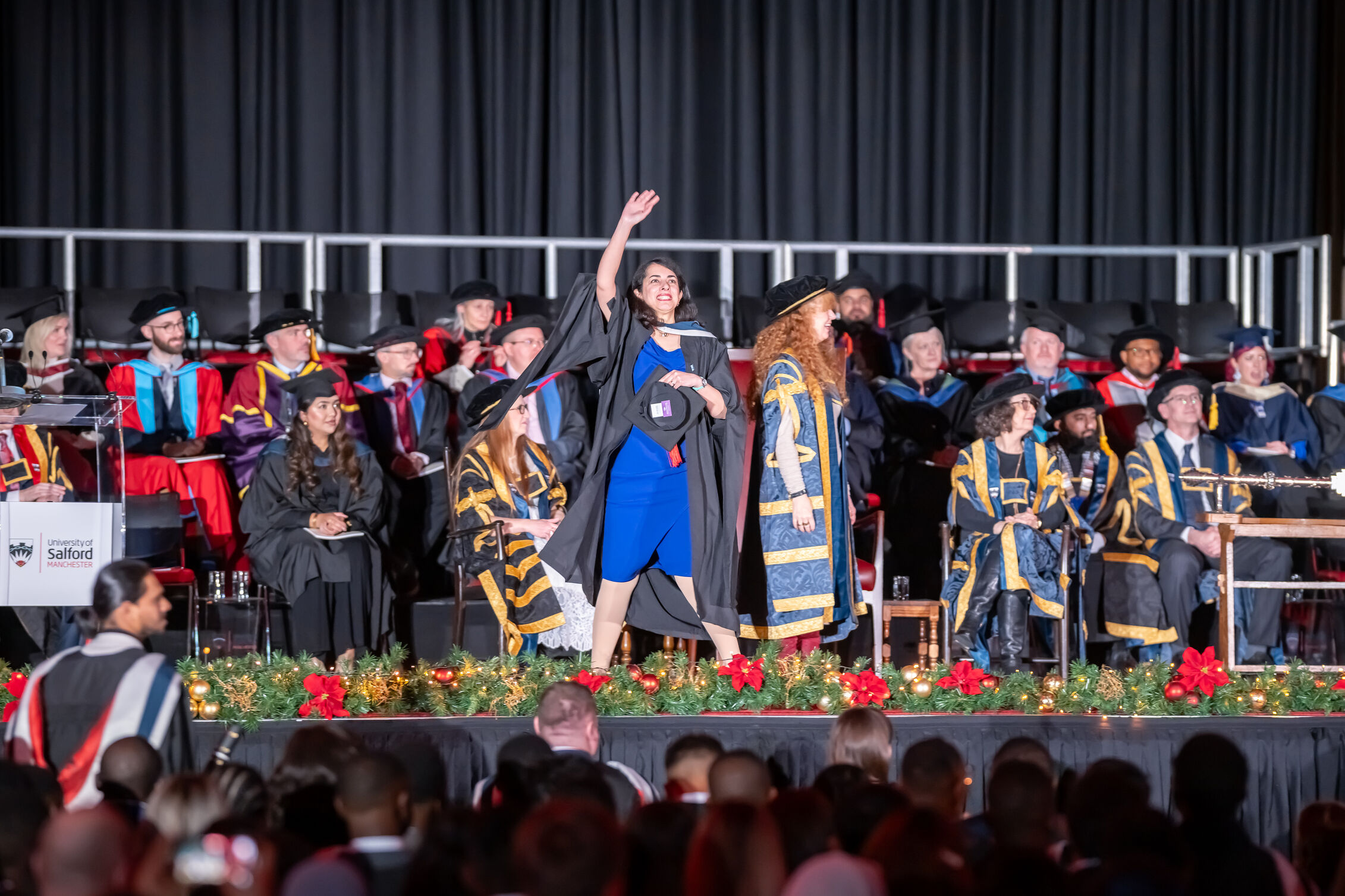 Graduate waves to the audience as she crosses the Graduation stage 