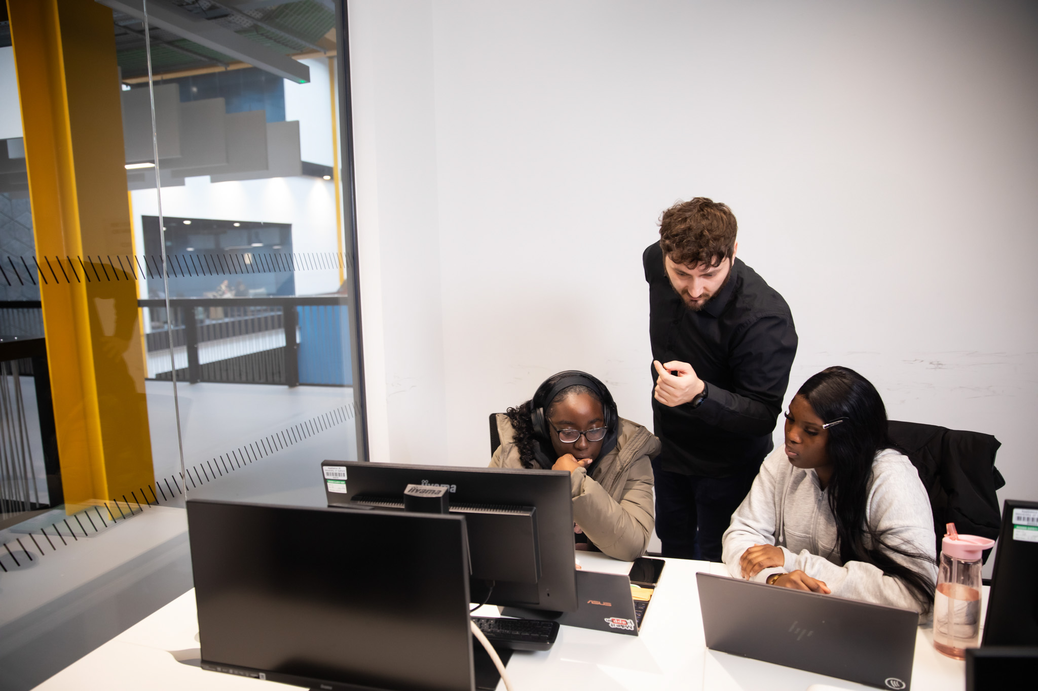 Tutor explaining to two students sat in front of computers