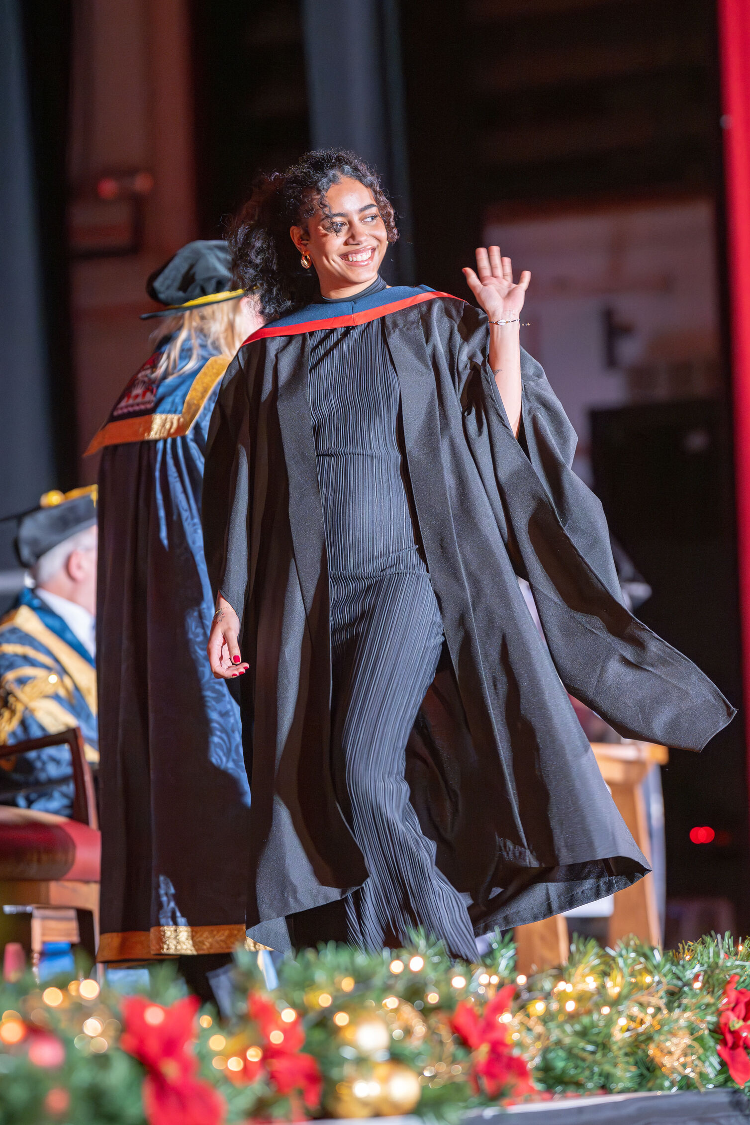 Graduate waves and smiles to the audience while walking across the graduation stage
