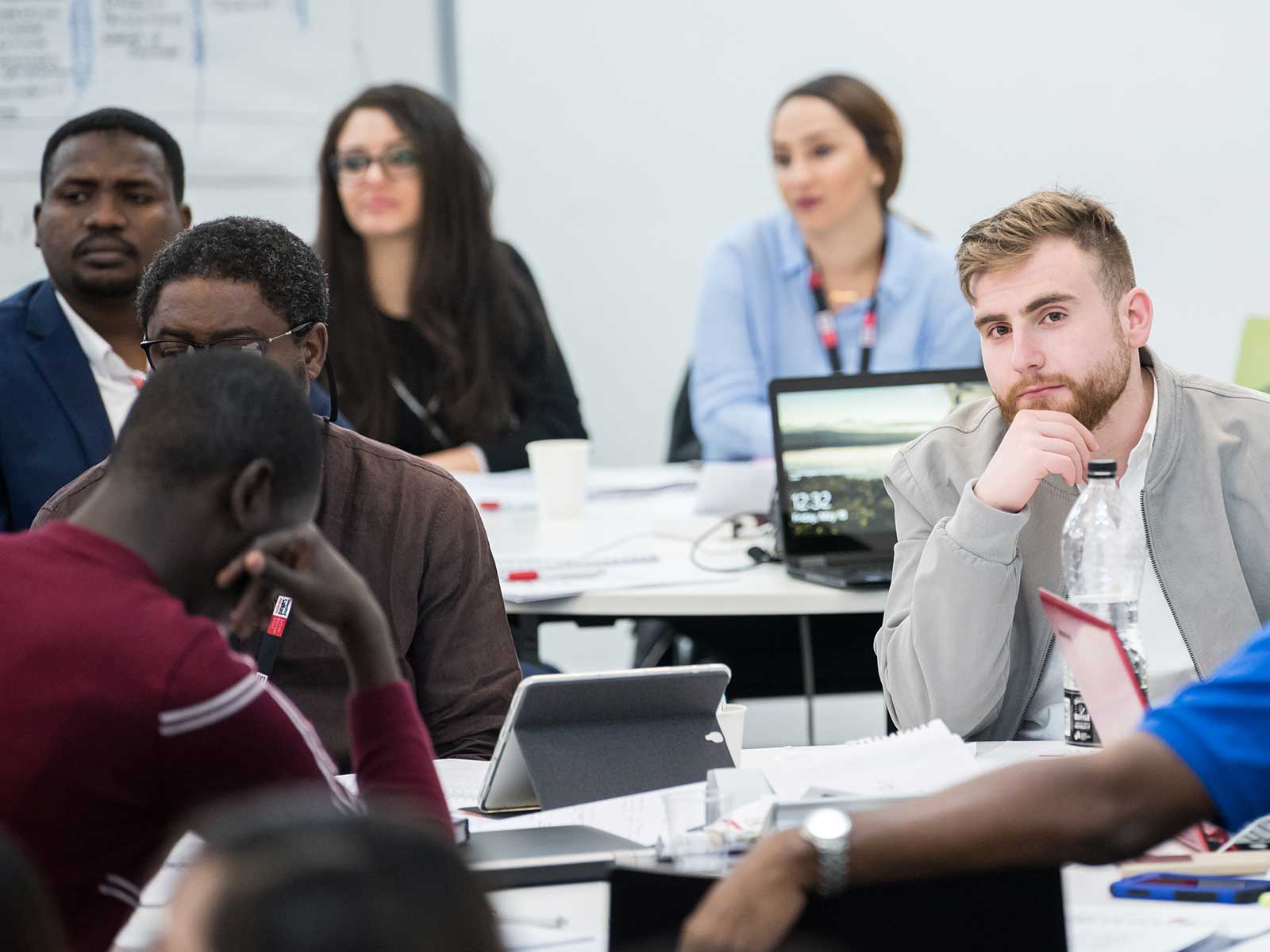 Six students in a lecture with laptops, tablets and note books