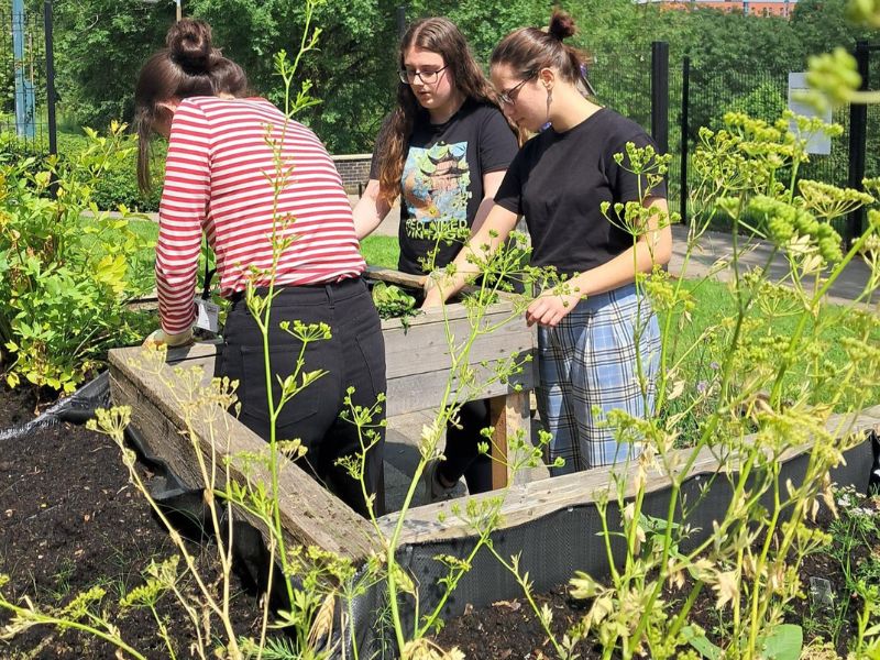 Three people digging into a planter at the Community Growing Space on a sunny day.