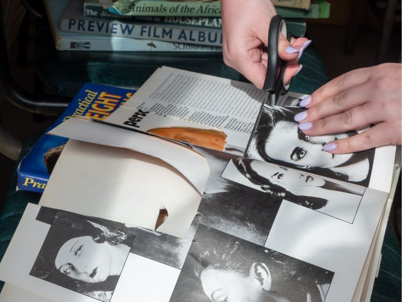 A pair of hands using scissors to cut some black and white images up and create a collage.