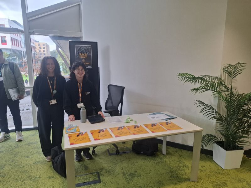 Two members of staff at a informational desk with cards on it