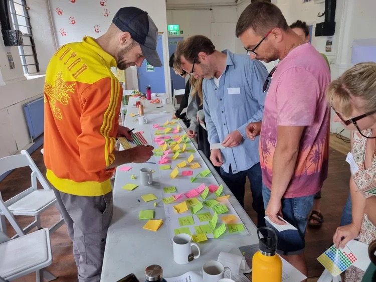 a group of people leaning over a long table looking at post stick notes with notes written on them