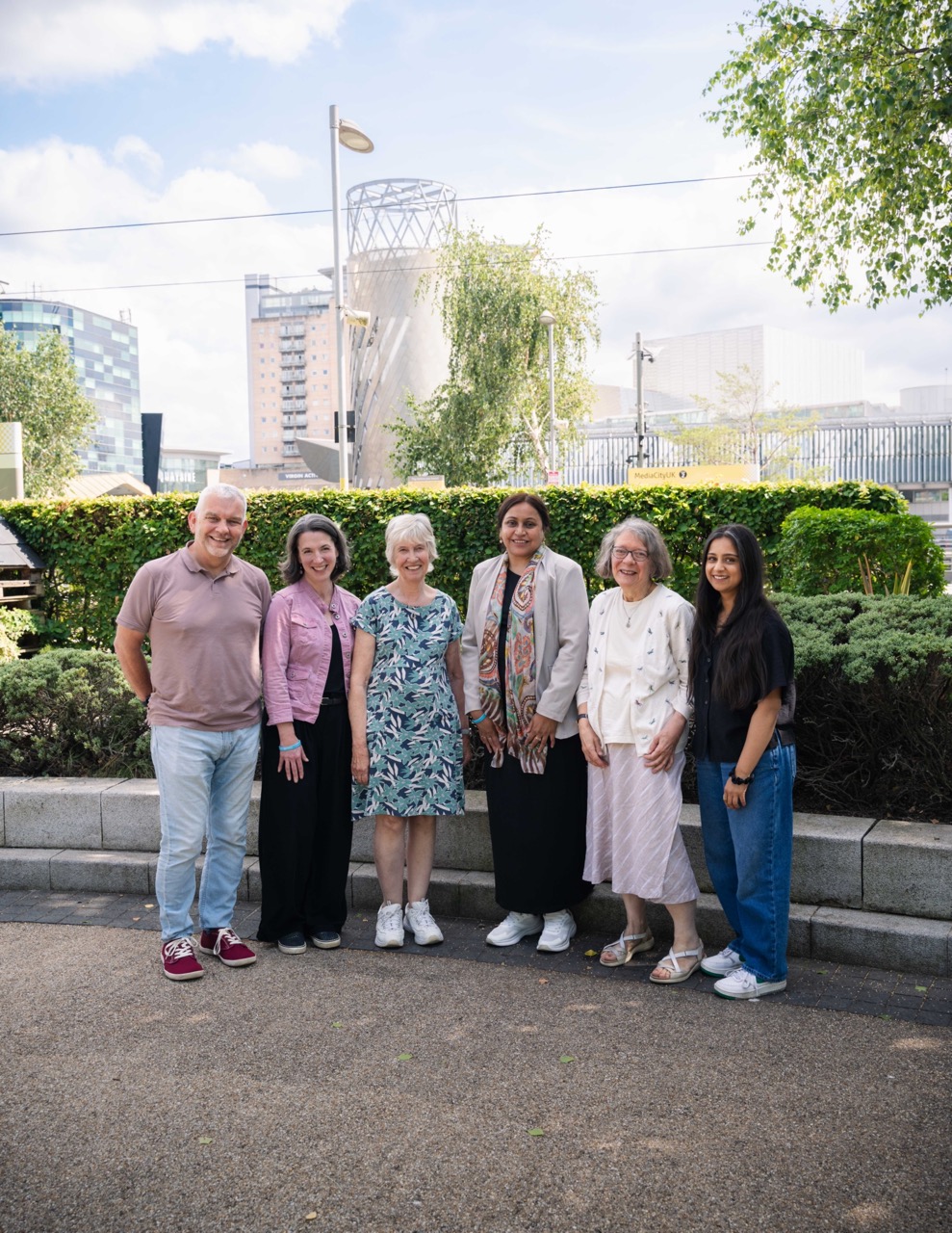 This image shows a group of people standing together outdoors, smiling at the camera