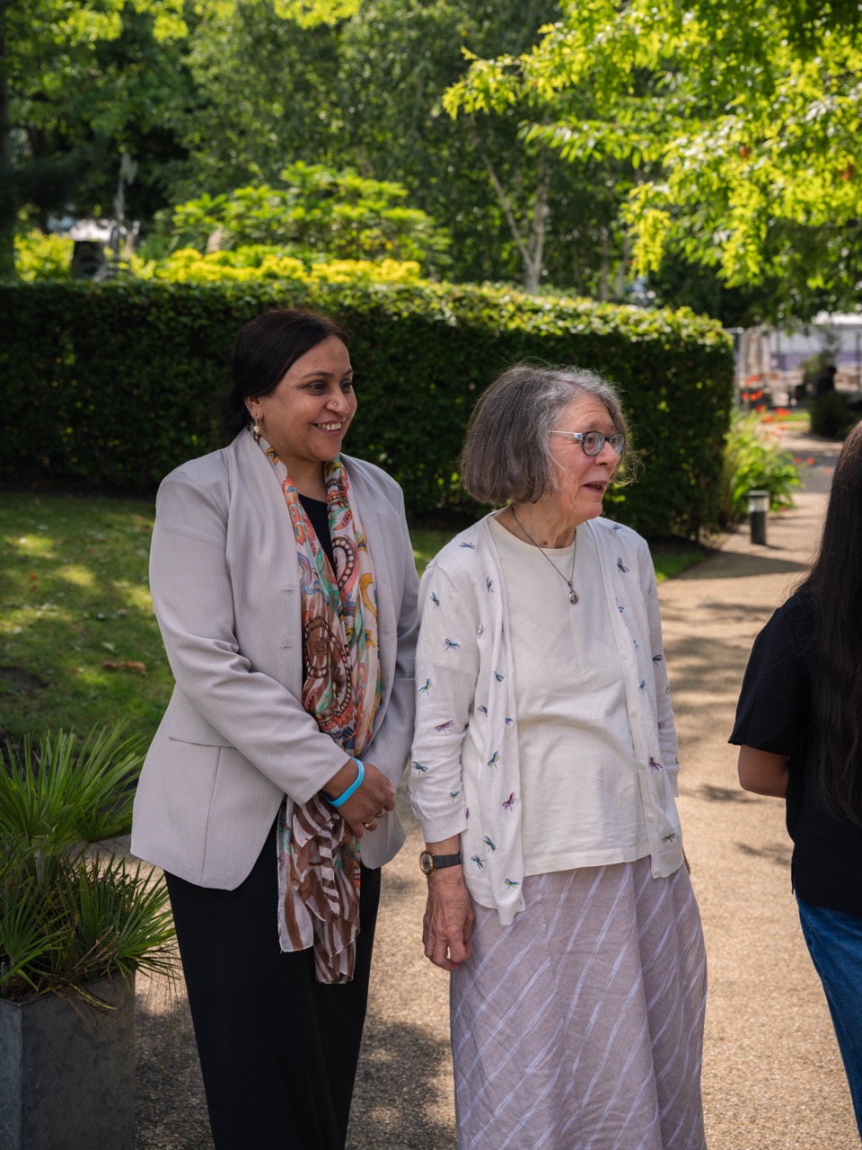 Two women, an older lady and a younger lady walking through a garden together. 