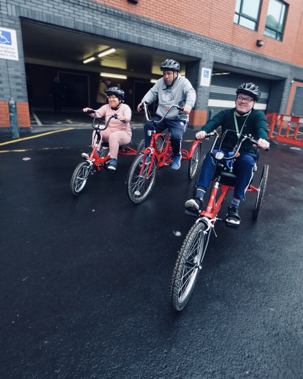 Three people riding adaptive tricycles down a street