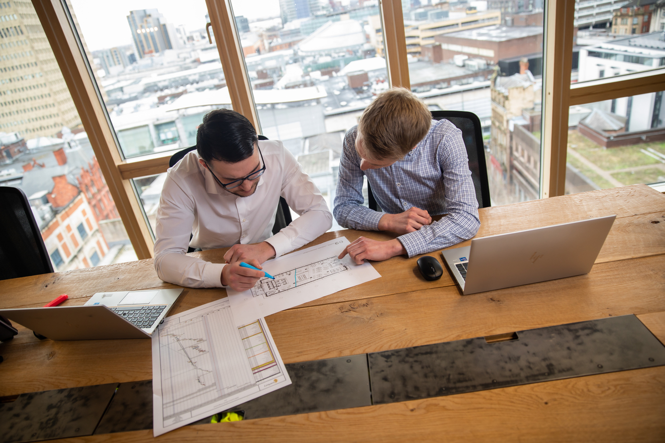 Two apprentices sit at a desk looking over construction plans