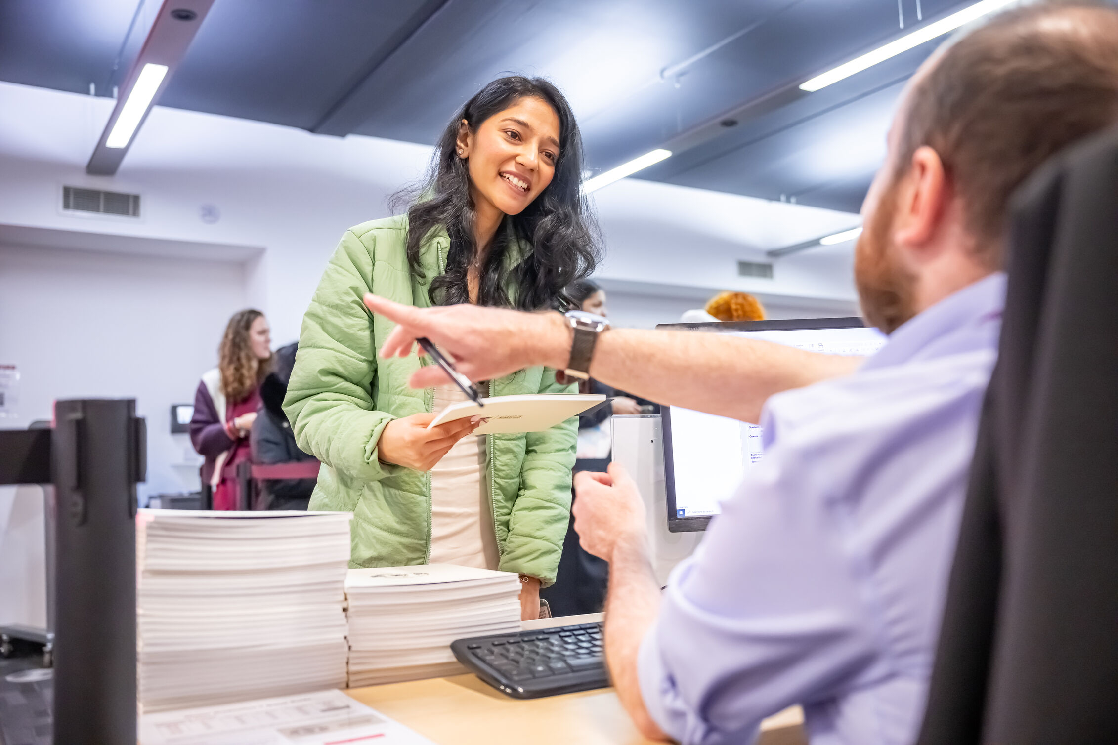 A person handing documents to a staff member across an information desk