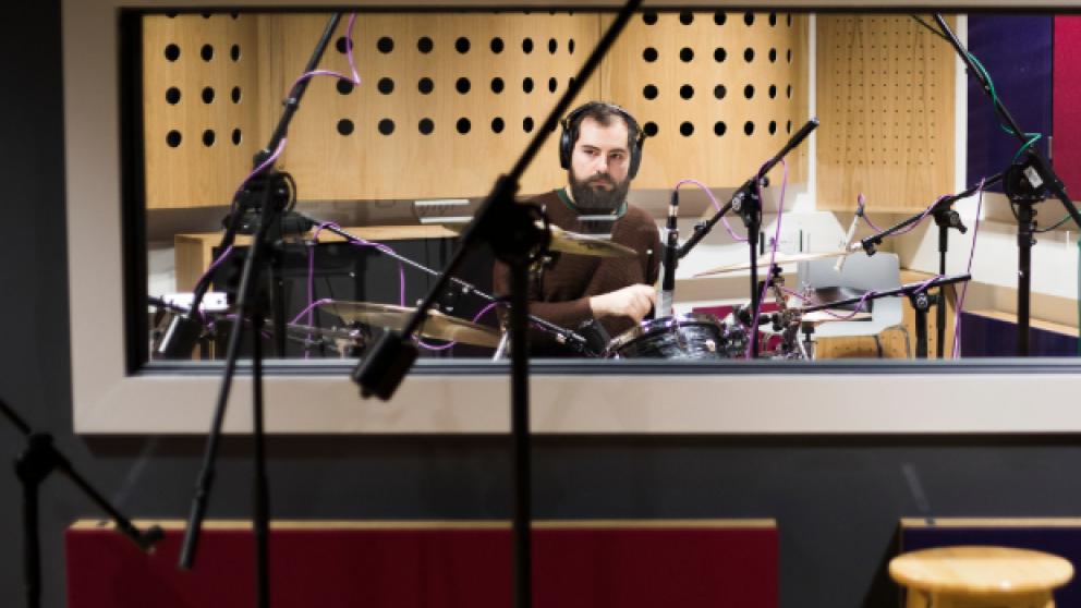 A Salford student plays the drums inside a recording booth.