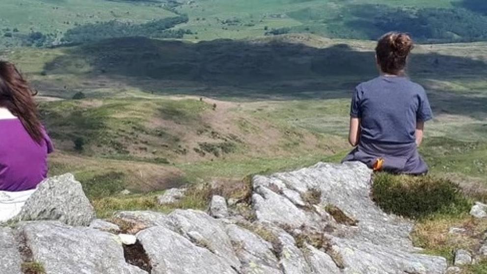 Two people sat on a rock outcrop looking at hills in the background