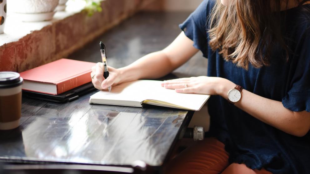 Woman sat at a desk writing in a notebook