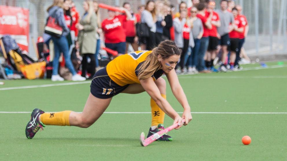 Group of students watching a hockey player about to hit a ball 