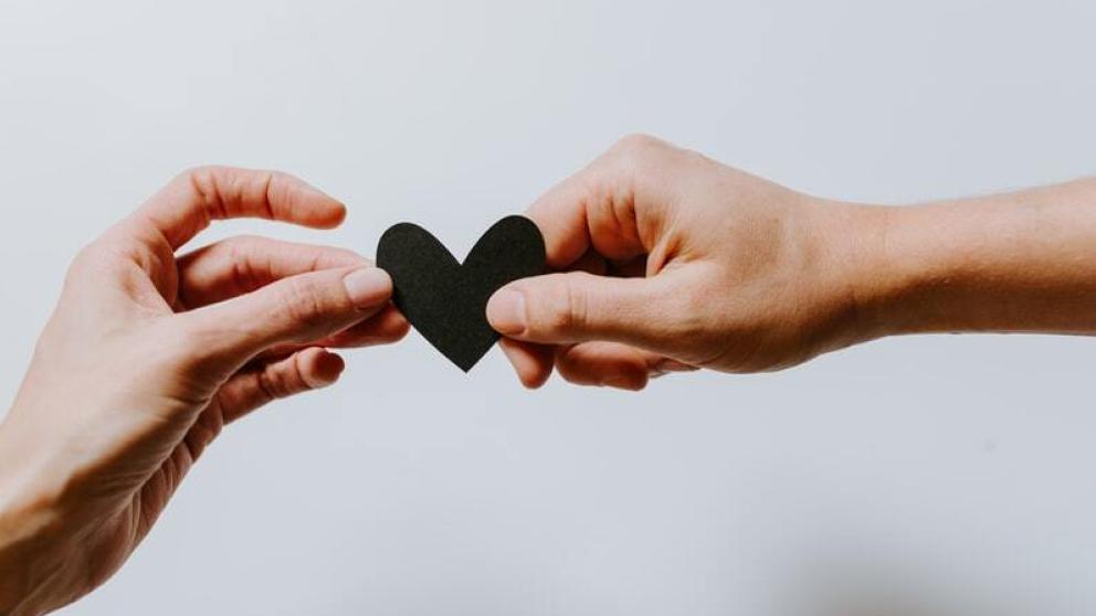A hand passing a black heart cutout to another hand