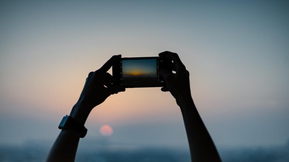 Pair of hands holding a mobile phone taking a sunset photograph