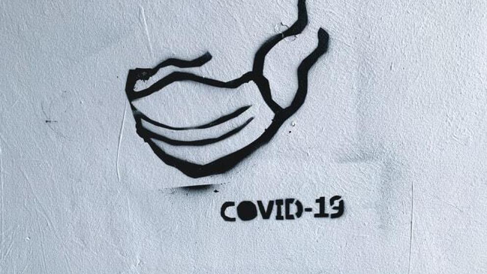 Spray-painted graffiti, outline of a face mask with the text "COVID-19"