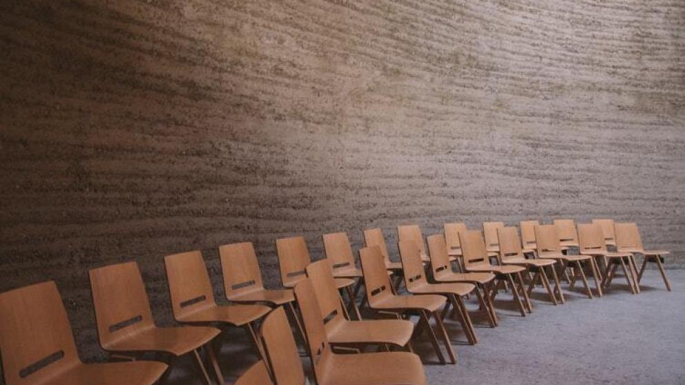 Room set up for a gathering, lecture, or workshop with rows of wooden chairs arranged in a semi-circle