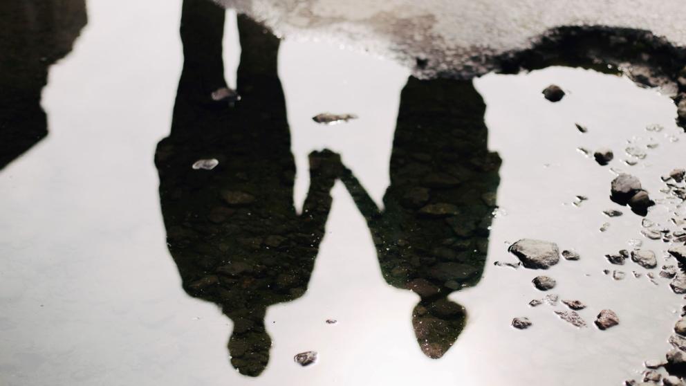 A couple holding hands as seen from the reflection of a puddle