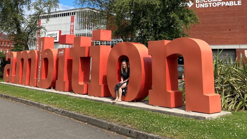 Sarah Garner sat inside the Ambition sign, University of Salford