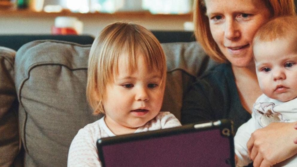 Mum sat on sofa watching iPad with her kids
