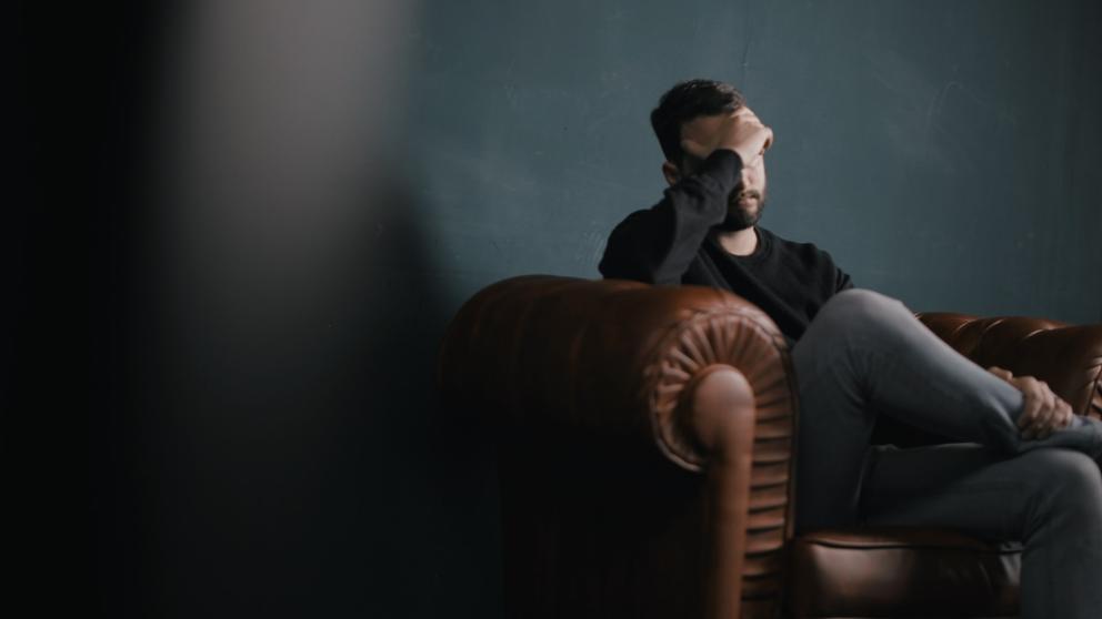 A man holds his head while sitting on a sofa