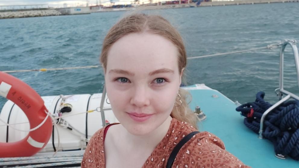 A landscape picture of Lucy as she takes a selfie with the seafront in the background.