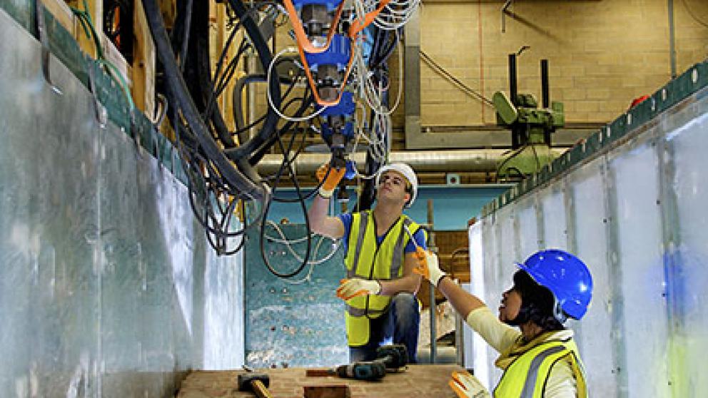 Two people wearing safety gear looking at a blue metal structure with cables attached 