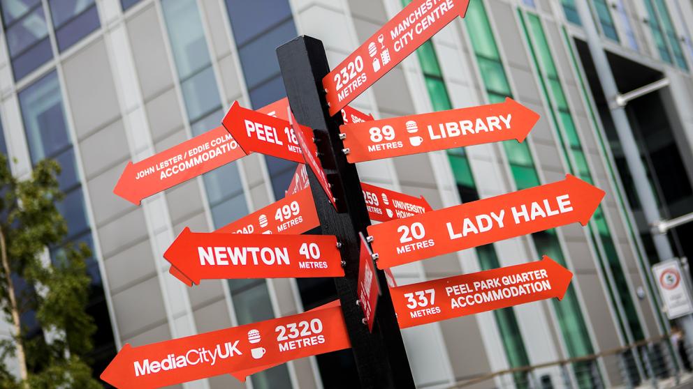 A red signpost showing destinations on Peel Park Campus, University of Salford