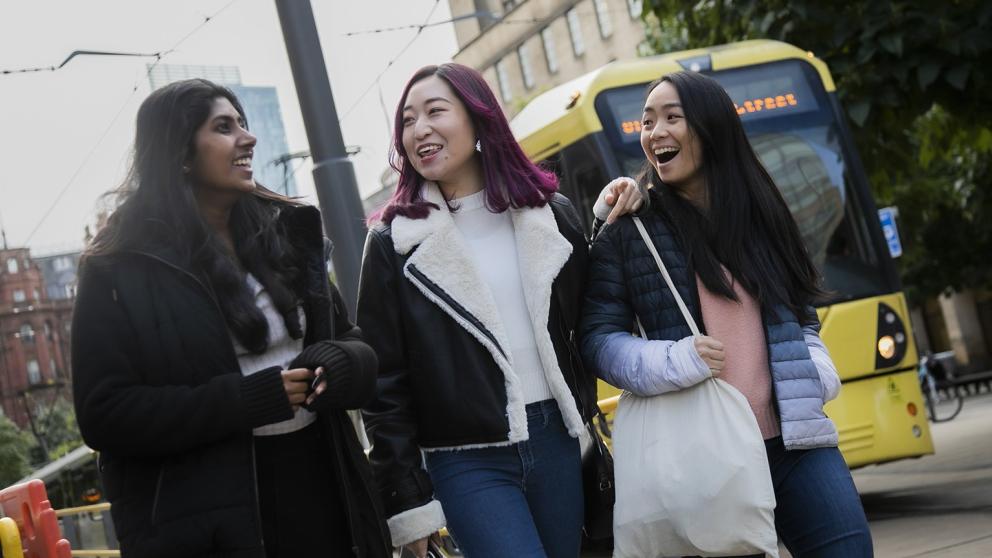Three students walking around Manchester city centre alongside a tram