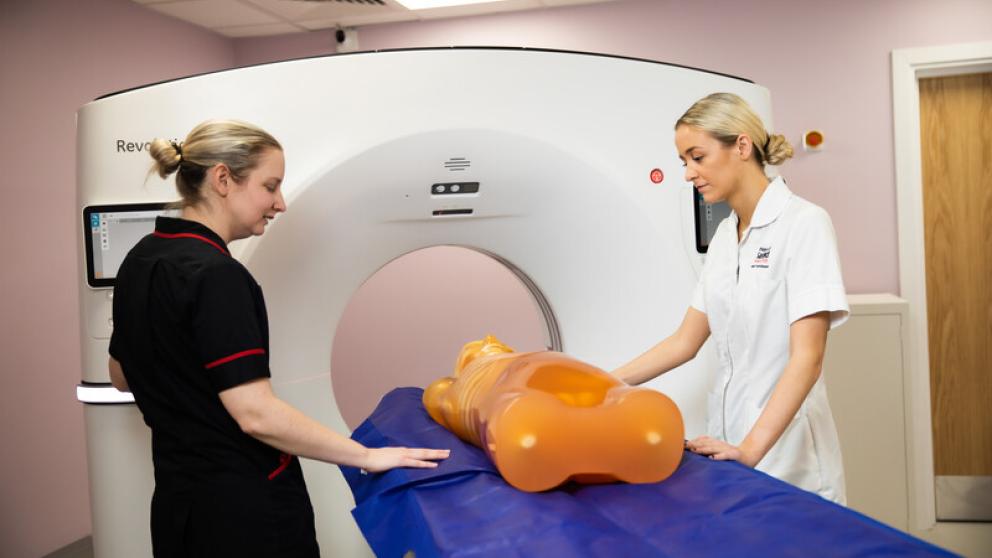 Two women in medical uniform performing an MRI on a plastic mannequin. 